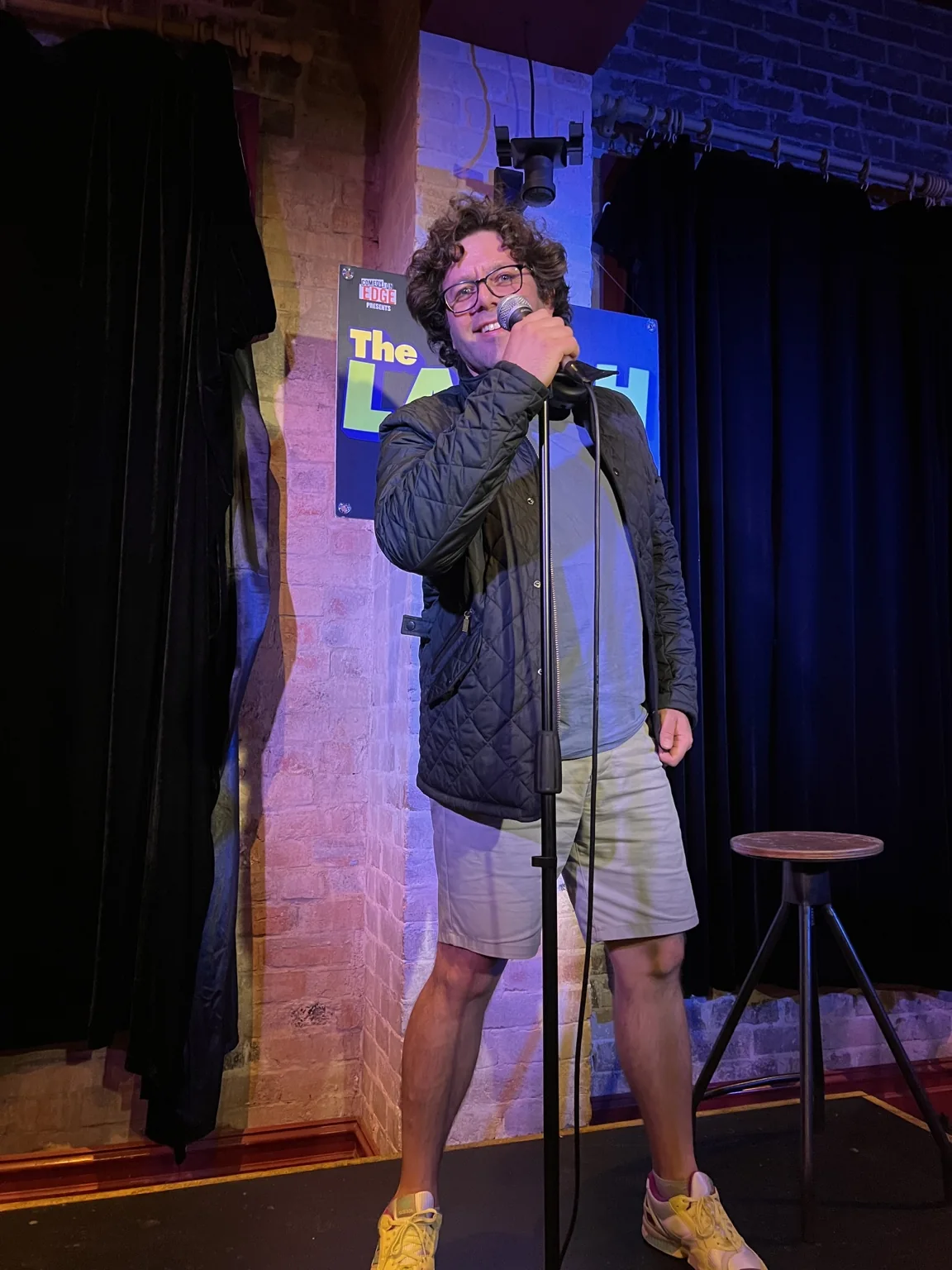 Artie Kay posing with a microphone on the stage at The Laugh Inn in Sydney in 2023, before ever performing stand-up